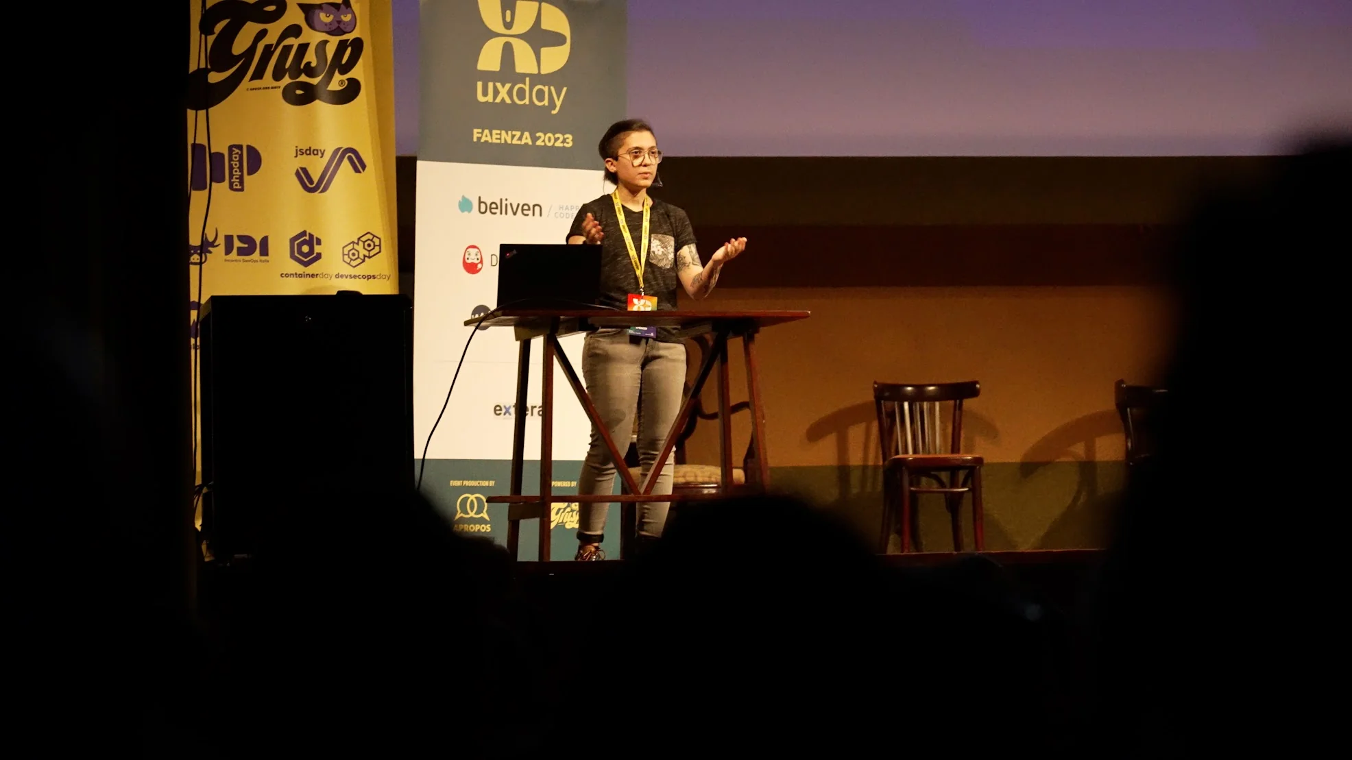 Valeria Salis speaking at UX Day 2023 in Faenza, Italy. Valeria has short hair and is wearing a black t-shirt and the coloured badge from GrUSP.